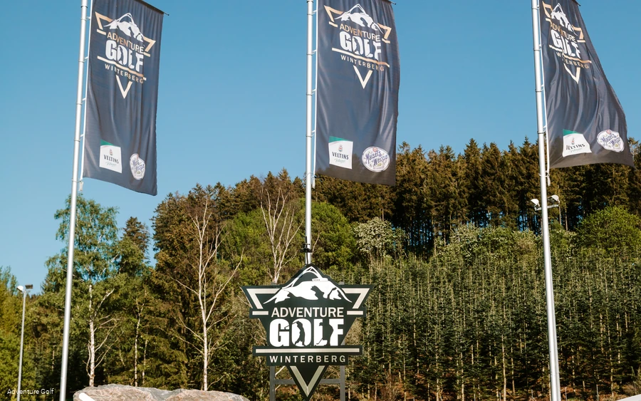 Drei Fahnen mit der Aufschrift Adventure Golf und einem Schild mit der selben Aufschrift.