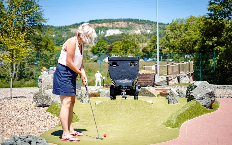 Eine Frau spielt Golf auf einer Bahn mit einem Bergwerk-Waggon als Hindernis.