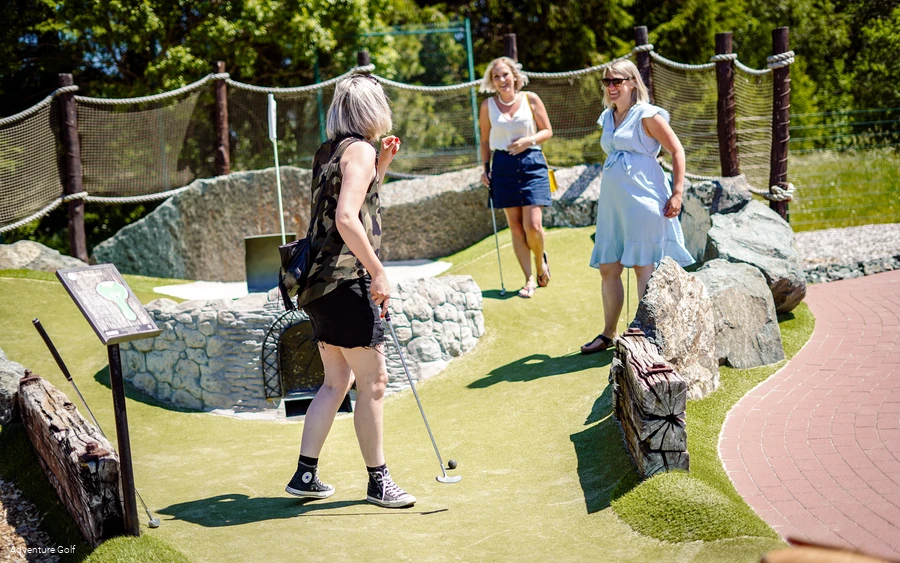 Mehrere Personen spielen Golf auf einer Bahn mit einer hölzernen Bikerampe als Hindernis.